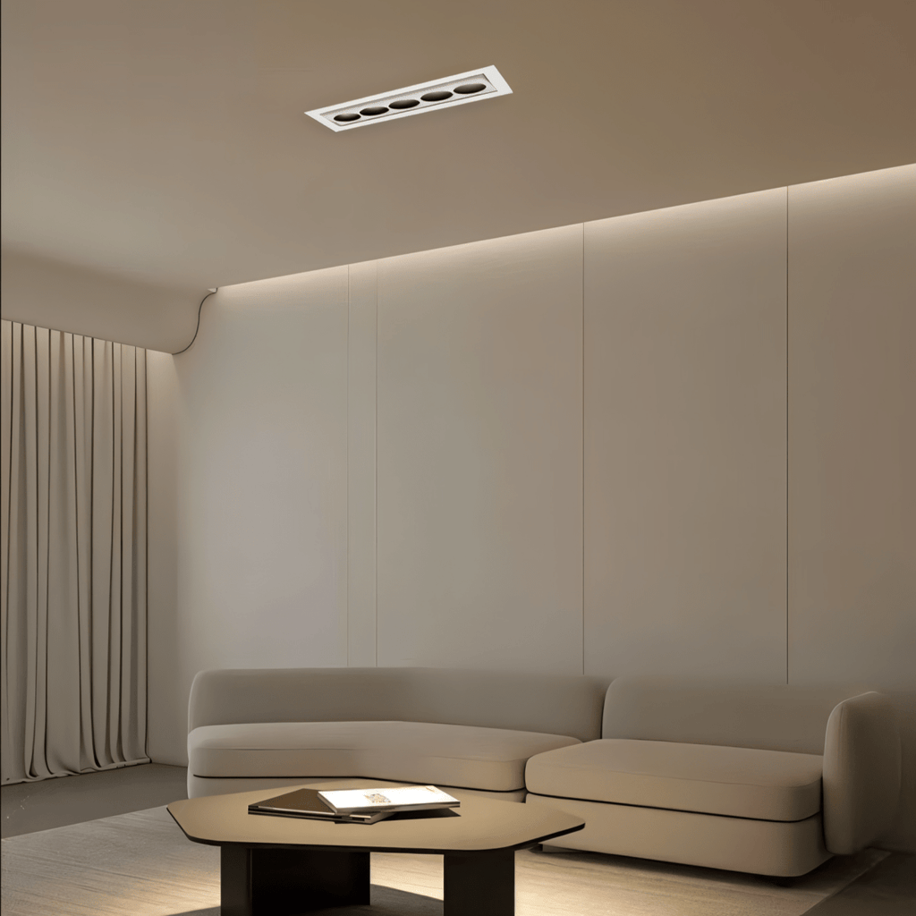 Clérachic five-reflector white recessed downlight in a taupe living room ceiling, with a cove glow above panelled walls and a low sofa.
