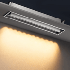 Clérachic recessed white linear downlight with its inner bar tilted to aim light, throwing a scalloped warm wash across a textured wall.