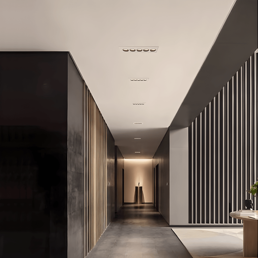 Clérachic white recessed linear downlights running down a dark corridor ceiling towards a lit alcove and slatted walls.