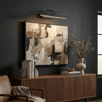 Black Clérachic wall light hung above a large abstract canvas on a dark wall, over a walnut sideboard and a leather chair.