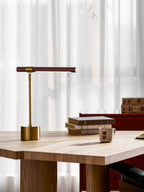 Low-angle view of this Clérachic desk lamp on a pale oak table, its walnut bar level above a stack of books and a cup.