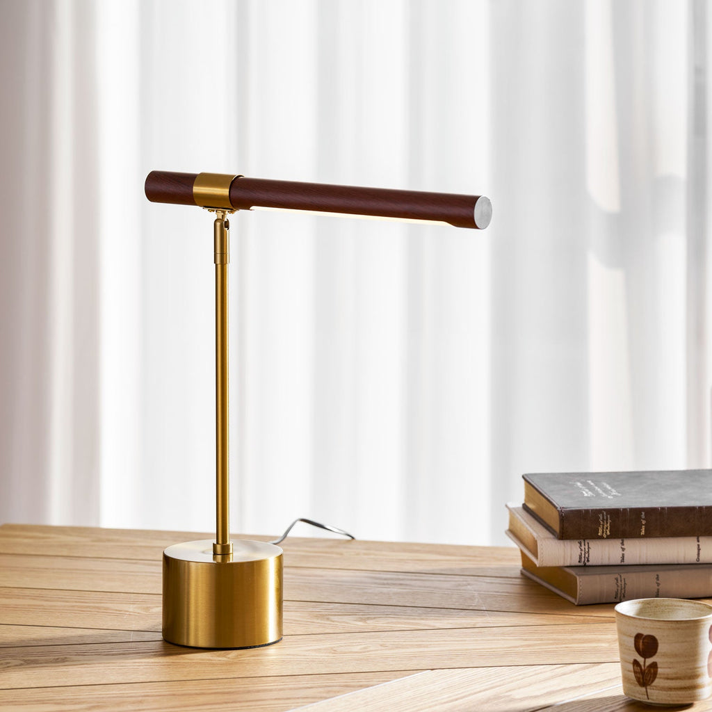 Close framing of this Clérachic lamp on an oak desk, its brass base and stem rising to a walnut bar against white curtains.