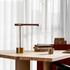 Clérachic desk lamp at the edge of a wide oak table, with a pile of books and a small cup beside the brass base.