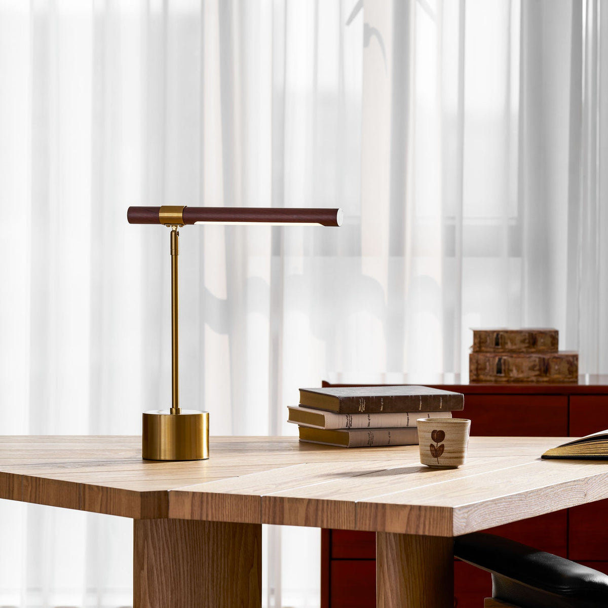 Clérachic desk lamp at the edge of a wide oak table, with a pile of books and a small cup beside the brass base.