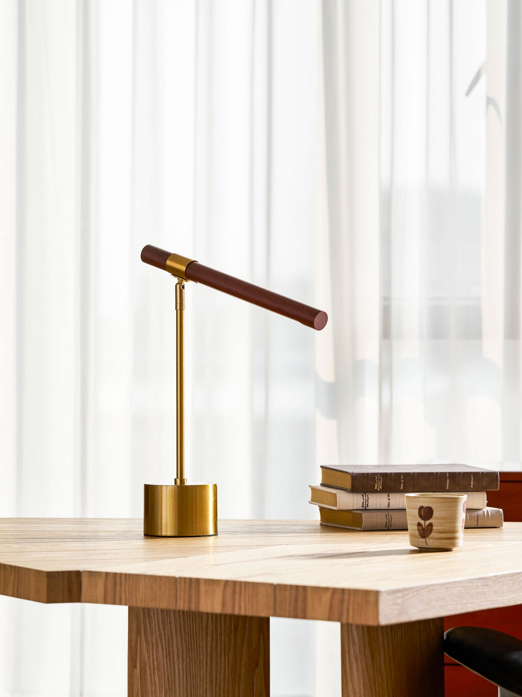 Smaller view of this Clérachic table lamp on a pale desk, its bar tipped down at one end, with books and a cup nearby.