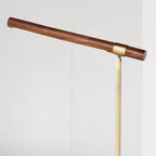 Walnut bar tilted across the frame on this Clérachic lamp, with a thin line of light along its underside and a brass stem below.