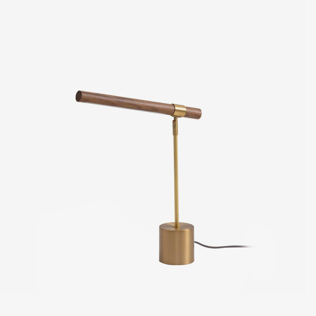 Clérachic table lamp on white, its walnut bar set at a slight angle over a brass stem, with the cord trailing from the base.