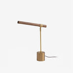 Clérachic table lamp on white, its walnut bar set at a slight angle over a brass stem, with the cord trailing from the base.