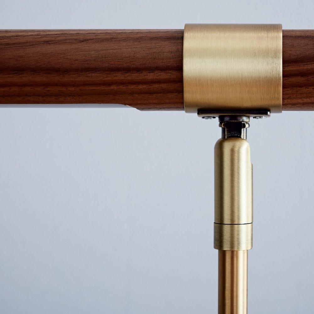 Close view of the brushed brass collar and joint holding the walnut bar on this Clérachic lamp, against a pale blue background.