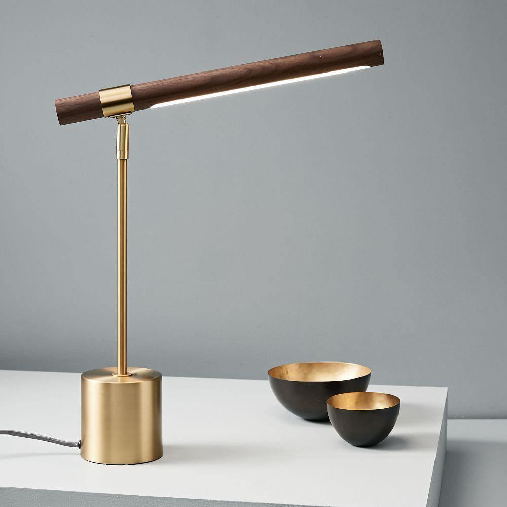 Lit Clérachic lamp on a white table against a blue-grey wall, its bar angled up, with two dark bowls with gold insides beside it.