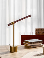 Clérachic table lamp on a herringbone desk, its bar raised towards a window of white curtains, with a stack of books to the right.