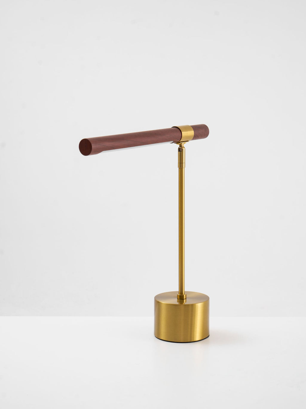 Clérachic table lamp on a white surface, a slim walnut bar tilted gently above a round brass base.