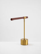 Clérachic table lamp on a white surface, a slim walnut bar tilted gently above a round brass base.