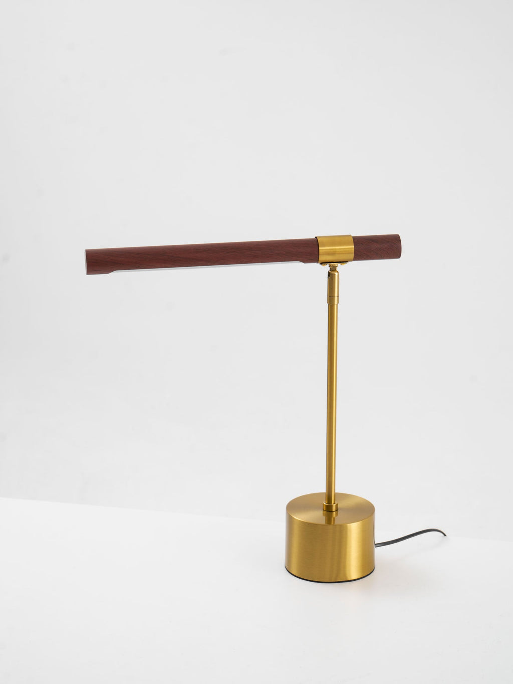 Clérachic lamp on a white surface, with a level walnut bar, brass stem and a grey cord leaving the base.