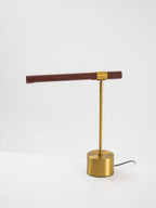 Clérachic lamp on a white surface, with a level walnut bar, brass stem and a grey cord leaving the base.