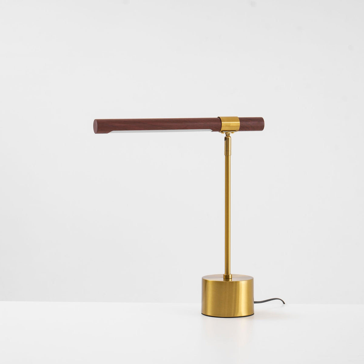 Front view of this Clérachic lamp on a white surface, its walnut bar almost level and the cord trailing off to the right.