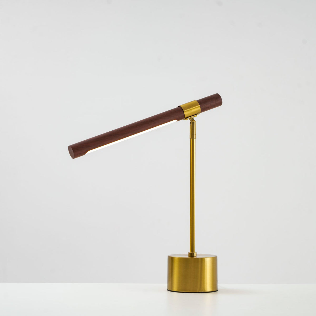 Clérachic table lamp with the bar tilted upward on its swivel, shown on a pale backdrop with a round brass base.
