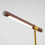 Close view of the lit strip under the walnut bar of this Clérachic lamp, with the brass collar and stem at the right.