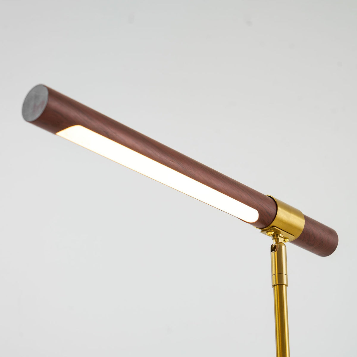 Close view of the lit strip under the walnut bar of this Clérachic lamp, with the brass collar and stem at the right.