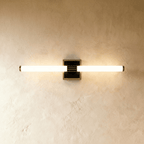 Clérachic LED tube wall light on a square black plate with a ribbed bronze-toned centre clamp, lit on plaster.