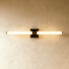 Clérachic longer LED tube wall light on a square black plate with a bronze-toned rim, glowing against plaster.