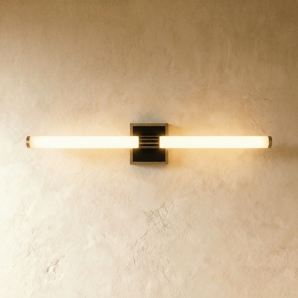 Clérachic longer LED tube wall light on a square black plate with a bronze-toned rim, glowing against plaster.