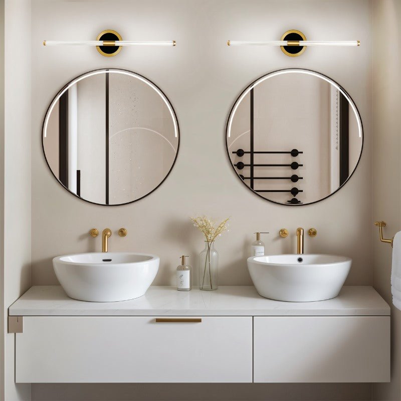 Pair of Clérachic LED tube wall lights on round brass plates above two round mirrors and white basins in a bathroom.