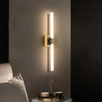 Clérachic LED tube wall light on a square brass plate, mounted vertically beside a bed with a tray of cups on the table.