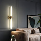 Clérachic LED tube wall light mounted vertically on a round brass plate in a grey panelled living room beside a sofa.