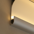 Clérachic silver aluminium profile light on a textured wall, with a curved lip and an open channel washing warm light upward.