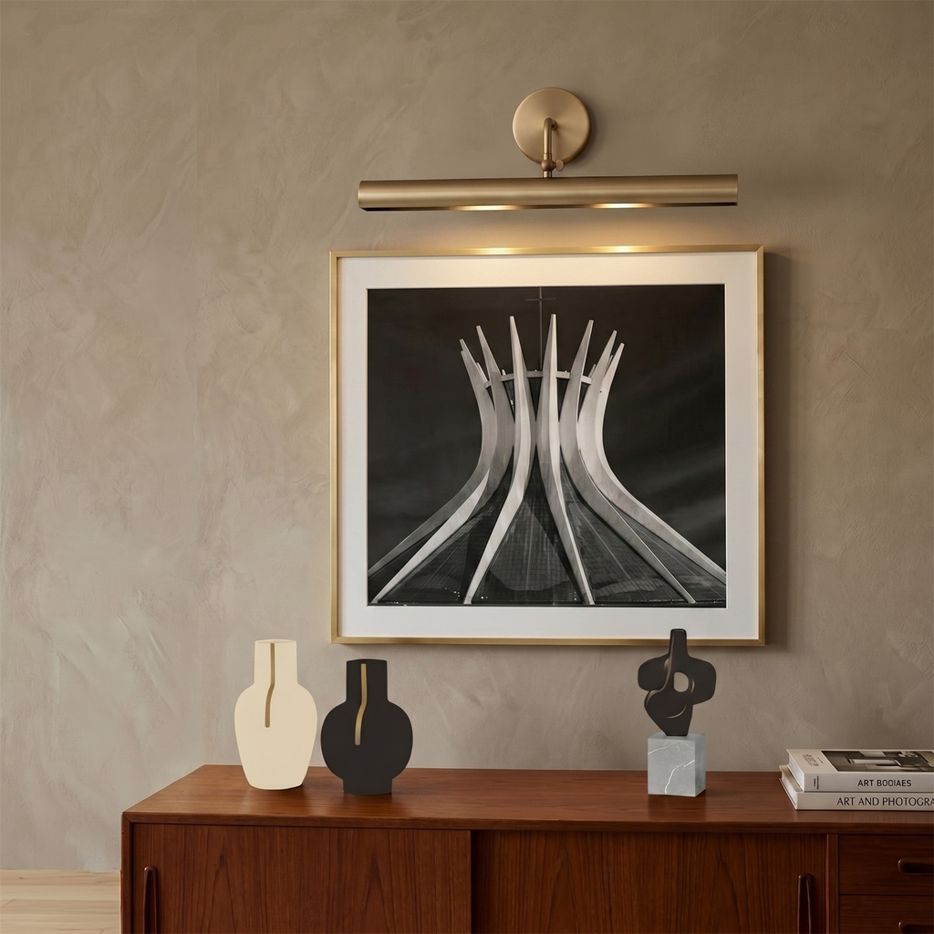 This Clérachic linear sconce lights a framed black-and-white sculpture print above a walnut sideboard with dark vases.