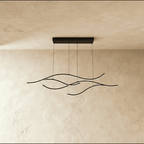 Clérachic black wave-shaped LED pendant with four slim glowing arcs on a rectangular canopy, hung against a limewash wall.