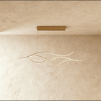 Clérachic gold wave-shaped LED pendant with four slim aluminium arcs hanging from a gold canopy on a limewash wall.