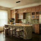 Clérachic black two-arc wavy LED pendant hanging over a marble kitchen island with oak cabinets and wooden stools.