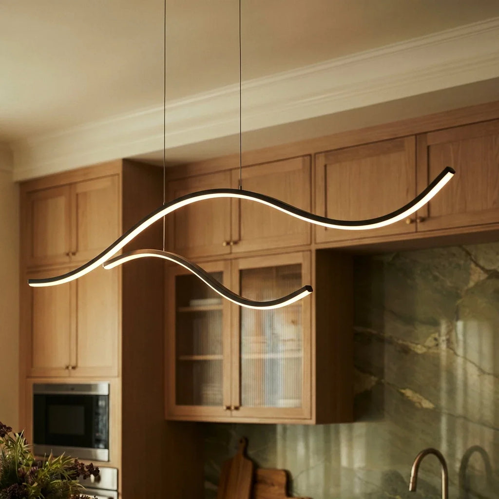 Close view of a Clérachic black wavy LED pendant, two glowing arcs on thin black cables in front of oak kitchen cabinets.