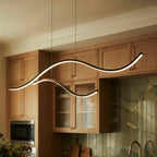 Close view of a Clérachic black wavy LED pendant, two glowing arcs on thin black cables in front of oak kitchen cabinets.