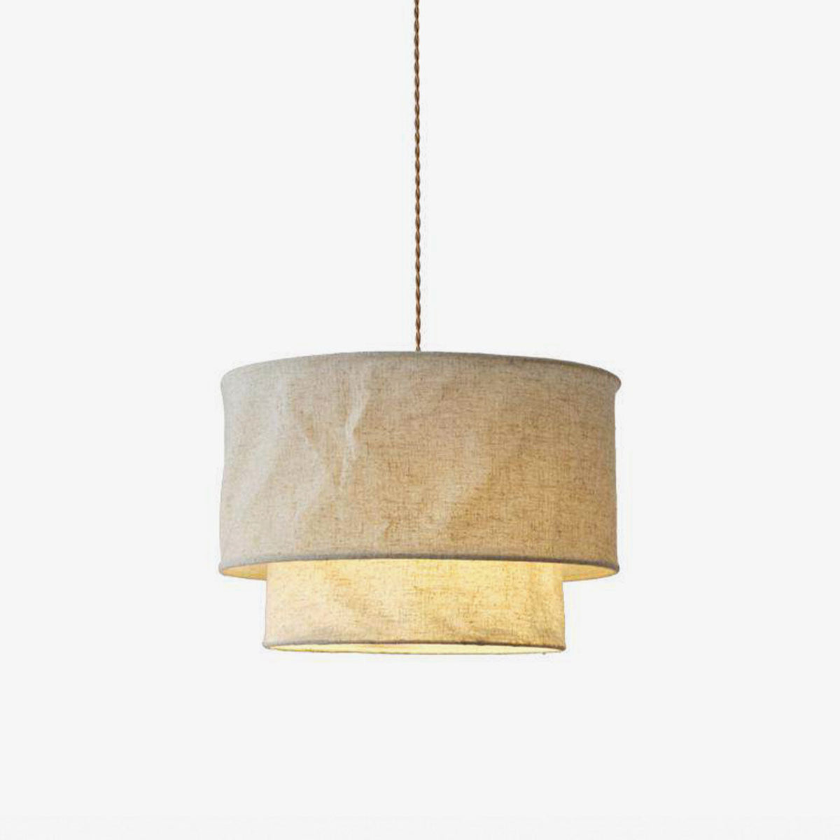Studio view of this Clérachic pendant's two-tier linen drum shade, glowing warm on a plain backdrop.