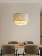 Over a wood dining table with green upholstered chairs, this Clérachic pendant glows against a plain wall.