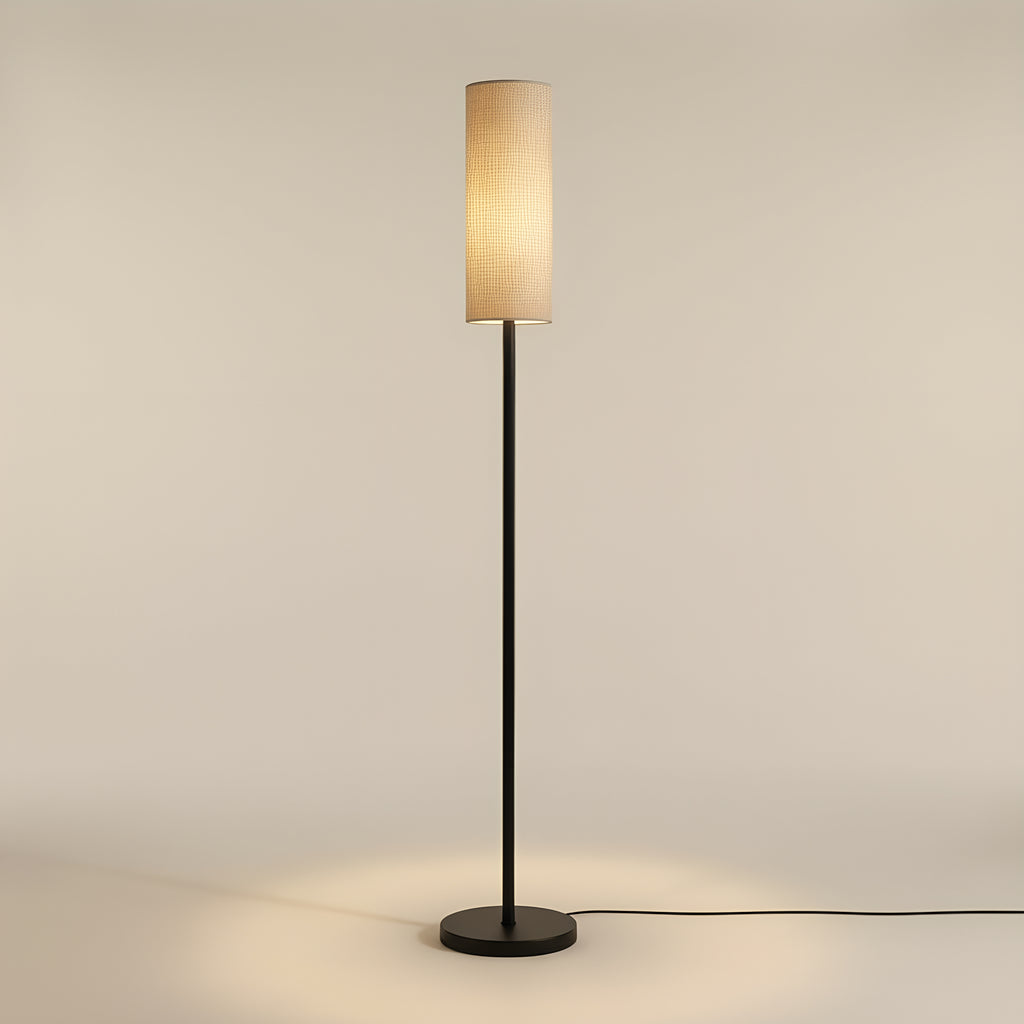The floor lamp at three-quarter view, the woven texture of the natural linen shade and the matte black finish of the pole clearly visible