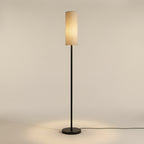 The floor lamp at three-quarter view, the woven texture of the natural linen shade and the matte black finish of the pole clearly visible