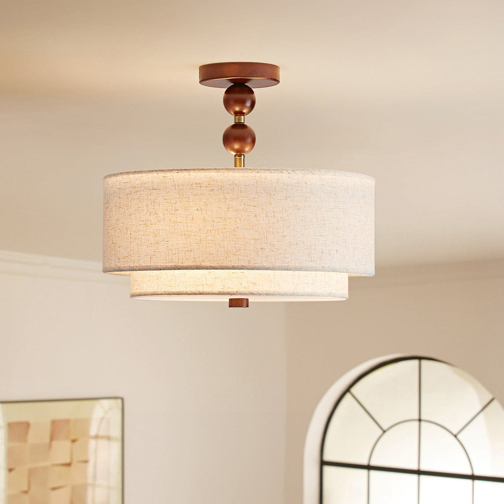 Lit Clérachic walnut-and-linen ceiling light with two stacked linen drums, seen against a cream wall and an arched window.