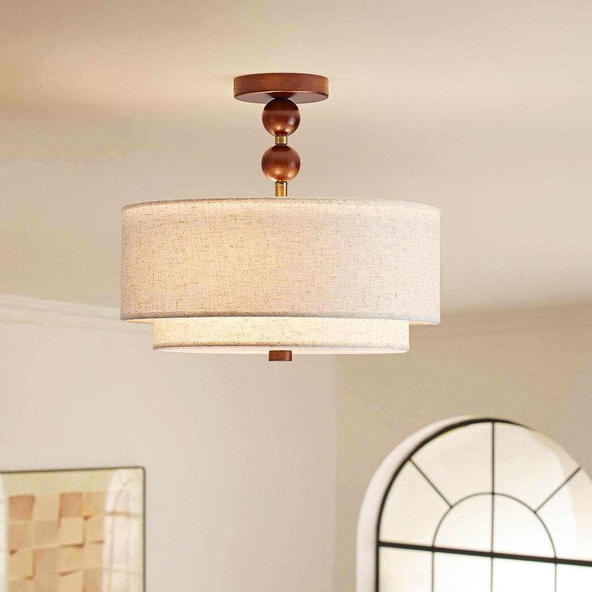Lit Clérachic walnut-and-linen ceiling light with two stacked linen drums, seen against a cream wall and an arched window.