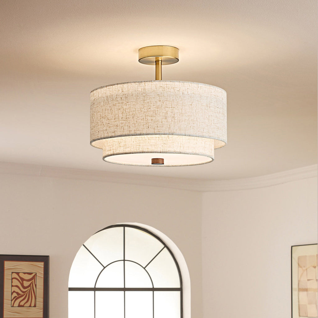 Clérachic ceiling light in the gold and linen finish, a slim brass stem above two linen drums, beside an arched window and framed art.