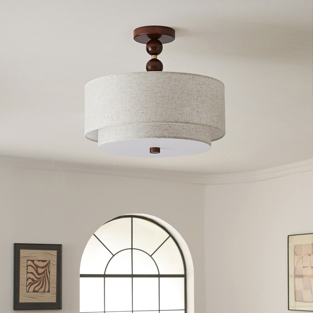 Clérachic walnut and linen double-drum light, switched off, below a curved cream ceiling with an arched window behind.