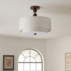 Clérachic walnut and linen double-drum light, switched off, below a curved cream ceiling with an arched window behind.
