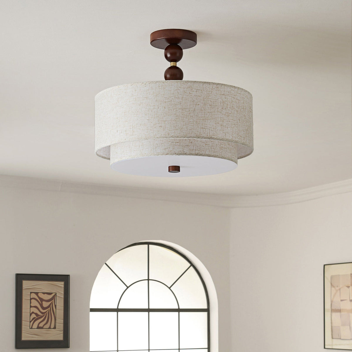 Clérachic walnut and linen double-drum light, switched off, below a curved cream ceiling with an arched window behind.