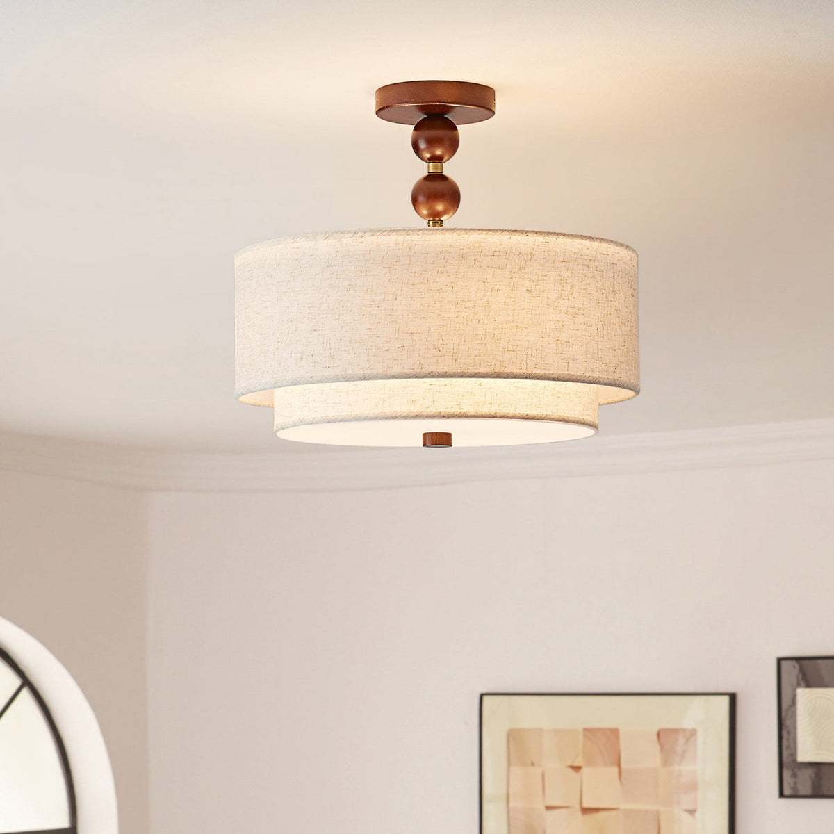 Clérachic walnut-ball stem and layered linen shade glowing softly above a framed picture and part of an arched window.