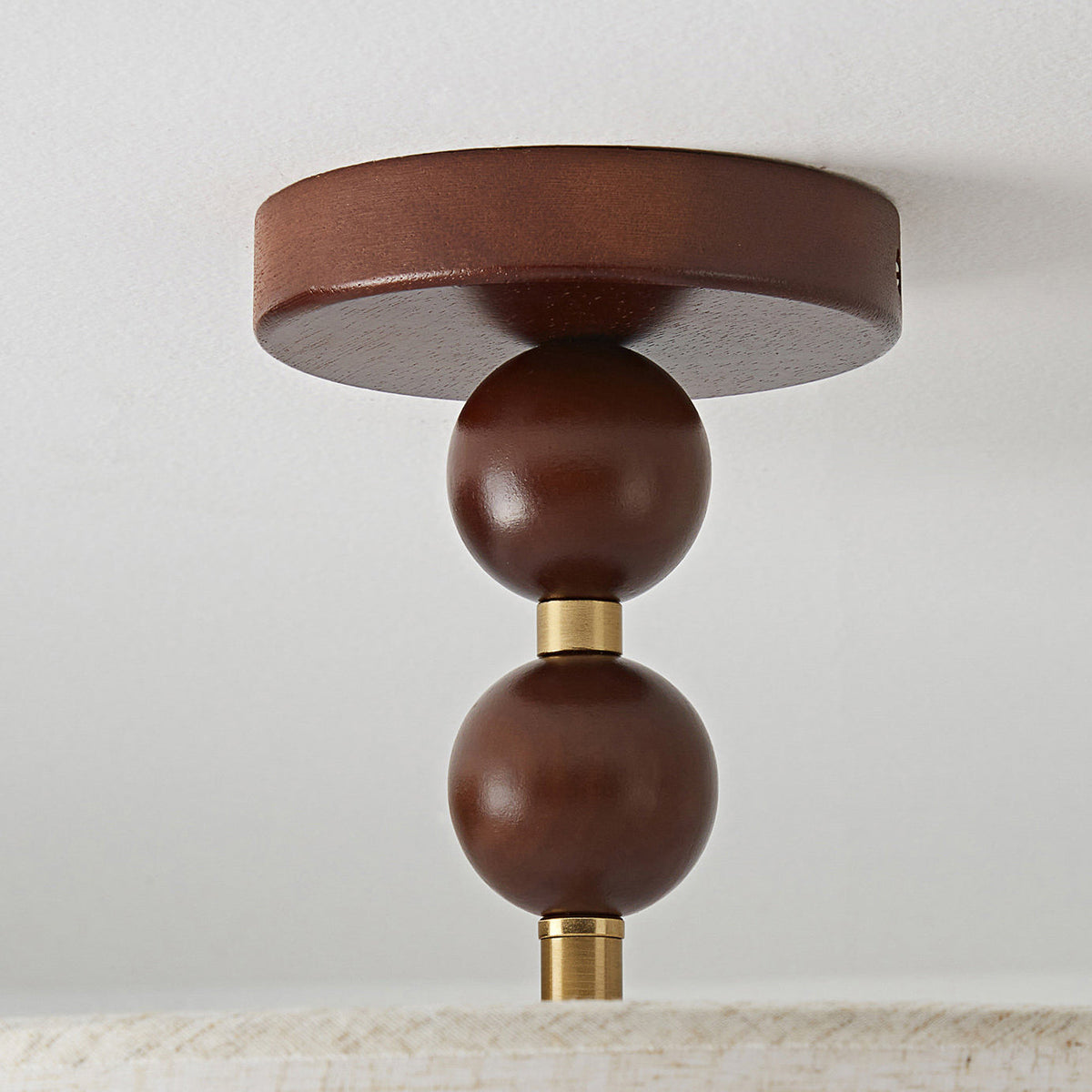 Close-up of the walnut-coloured canopy and two wooden balls with brass collars on this Clérachic flush-mount light.