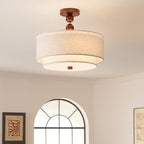 Warm-lit Clérachic double linen drum with a walnut ball stem, hung against a rose-cream wall and an arched window.