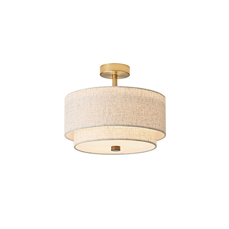 Clérachic ceiling light in gold and linen, with a round brass canopy, a short stem and a lit white diffuser underneath, on white.